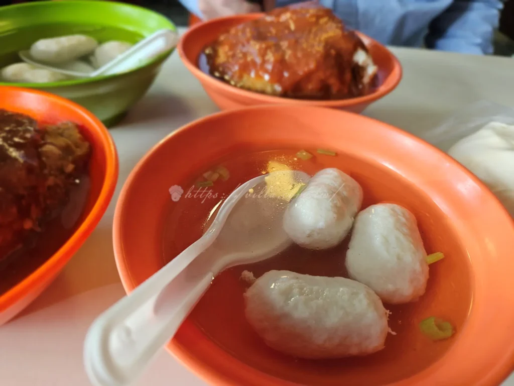 淡水文化阿給魚丸湯走的是清爽路線，魚丸彈中帶嫩，湯頭清甜，剛好平衡阿給的甜辣滋味，魚丸裡包了肉餡，一咬下去脆彈有汁，湯頭撒上一點芹菜末提味，喝起來溫潤不油膩。