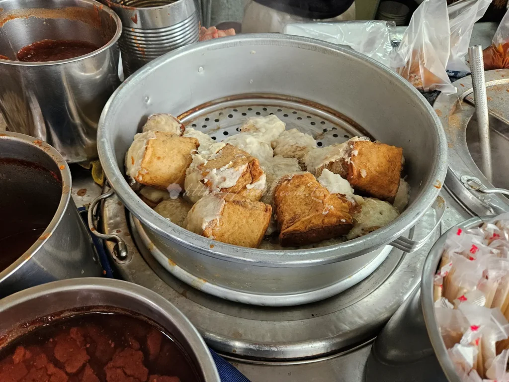 談起淡水的代表性美食，絕不能錯過坐落於真理街上的「文化阿給」。這道國民小吃的名字源自日語「油揚げ」（Abura-age）的諧音，意指油豆腐。相傳是由楊鄭錦文女士於1965年研發，最初是本著惜物精神，將滷好的冬粉填入油豆腐中並以魚漿封口，創造出層次豐富的飽足感。