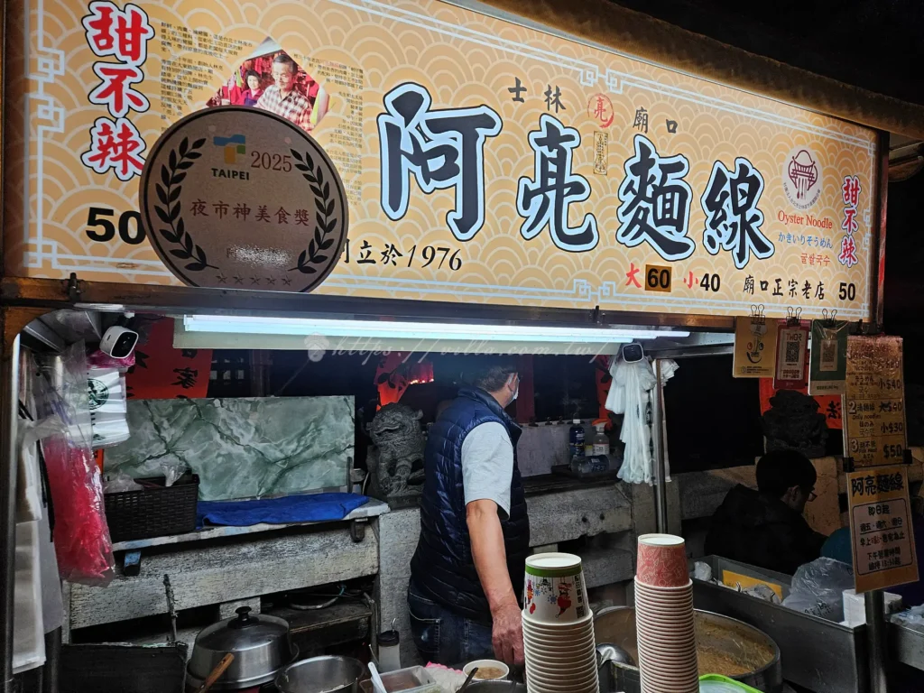 士林廟口老店阿亮麵線是讓很多台北人從小吃到大的士林老字號美食，飄香夜市超過半世紀以上，至今依舊維持那一碗樸實、勾芡濃郁的大腸蚵仔麵線風味，堪稱士林夜市必吃小吃之一。無論是本地人還是旅客，只要走過士林廟口這家麵線攤位前，都會不自覺停下腳步聞香而來。