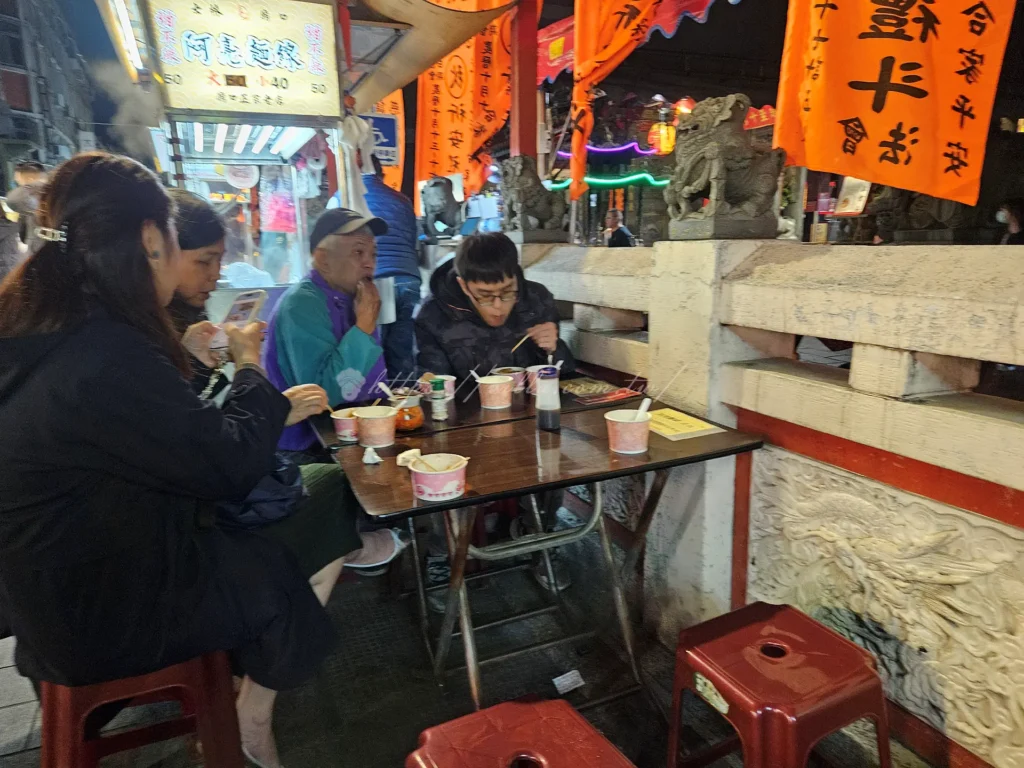 士林廟口老店阿亮麵線是讓很多台北人從小吃到大的士林老字號美食，飄香夜市超過半世紀以上，至今依舊維持那一碗樸實、勾芡濃郁的大腸蚵仔麵線風味，堪稱士林夜市必吃小吃之一。無論是本地人還是旅客，只要走過士林廟口這家麵線攤位前，都會不自覺停下腳步聞香而來。