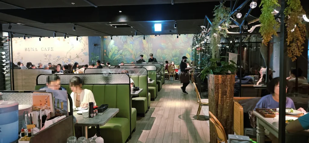 走進布納咖啡館(BUNA CAF’E)店內,首先會被挑高的空間與精緻的燈飾所吸引。這裡的裝潢融合了大量大理石與植栽,打造出名副其實的新北網美餐廳質感。最受歡迎的莫過於大片落地的玻璃窗位,陽光灑落時,窗外的公園綠意就像是一幅活生生的畫。這裡更是適合聊天聚會的餐廳,座位規劃多元,從適合單人辦公的插座座位到提供高質感包場空間的大型長桌應有盡有。