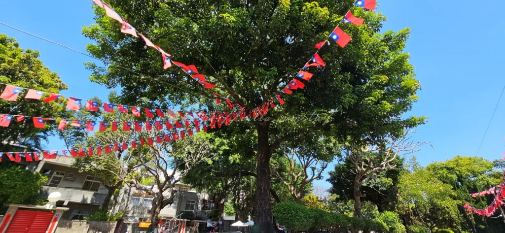 空軍三重一村的老榕樹廣場景點，陽光穿透樹蔭灑在木質休憩區，呈現出早期眷村鄰里在大樹下悠閒聊天、乘涼的溫馨懷舊氛圍。