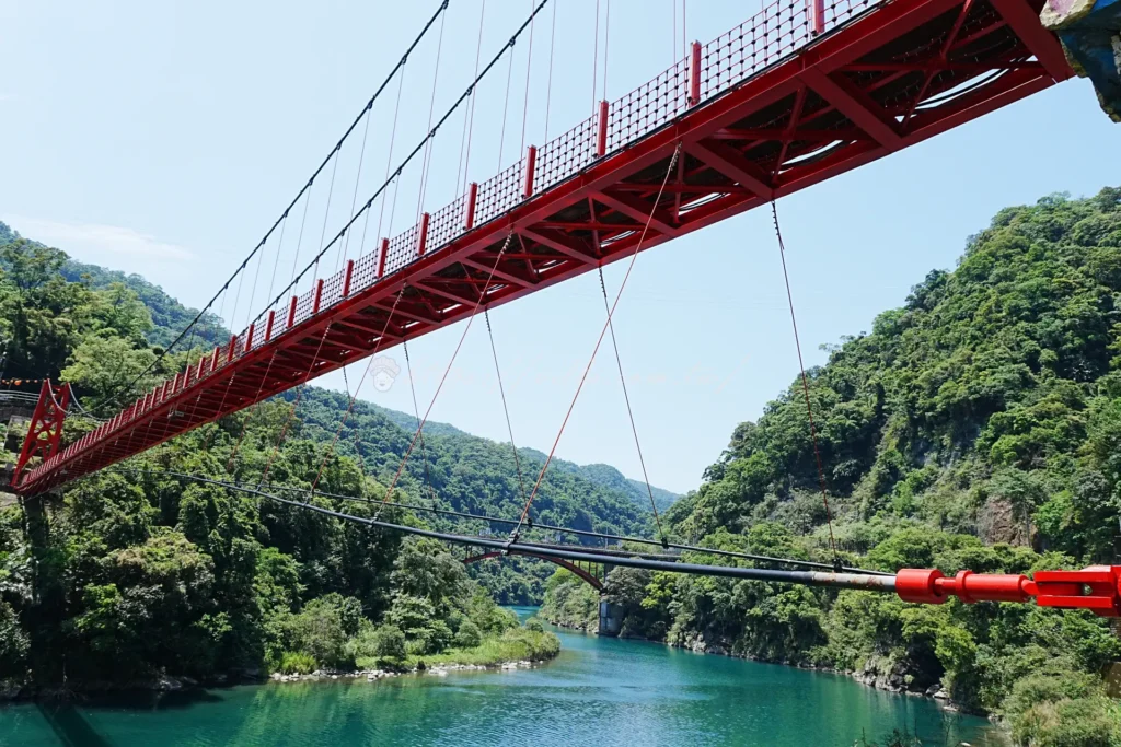 烏來吊橋下南勢溪溪水清澈見底，溪流在翠綠山林環抱中蜿蜒流淌，是烏來老街入口最美的自然風景